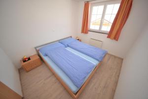 um pequeno quarto com uma cama com lençóis azuis e uma janela em Waluschi em Belalp
