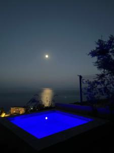 a blue swimming pool at night with the moon in the sky at Hotel Amare in Palasë