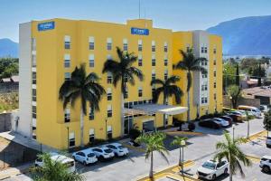 a yellow building with palm trees in a parking lot at City Express by Marriott Ciudad Victoria in Ciudad Victoria