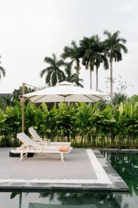 a pool with a white umbrella and chairs next to a swimming pool at Sadec Garden Boutique Hotel in Ấp Tân Thành (2)