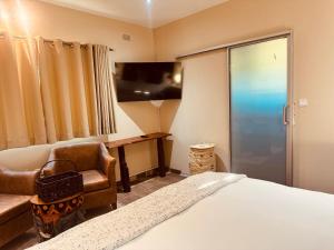 a bedroom with a bed and a chair and a tv at Wild Haven Lodge in Victoria Falls