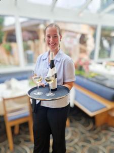 a woman holding a tray with a bottle of wine and glasses at Hotel Toggenburgerhof in Kirchberg