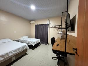 a room with two beds and a desk and a television at Pousada G3 in Presidente Figueiredo