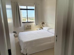 a bedroom with a white bed and a window at Flat Jardim de Allah in Campos dos Goytacazes