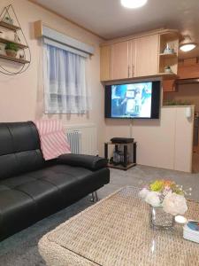 a living room with a black couch and a flat screen tv at Holiday Sea Caravan in Withernsea +16 photos