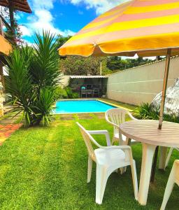 a table and chairs with an umbrella next to a pool at Suítes Colibri da Serra - Piscina & Conforto em Itaipava RJ in Itaipava