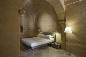 1 dormitorio con 1 cama en una pared de piedra en Antico Convicino Rooms Suites & SPA en Matera