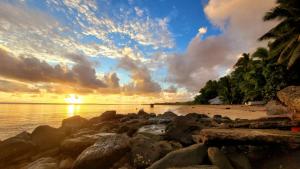 a sunset on a beach with rocks and palm trees at sandbar Homestay in Lautoka