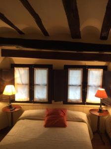 アルネディリョにあるCasa Rural Las Pedrolasのベッドルーム1室(窓3つ、ランプ2つ付きのベッド1台付)