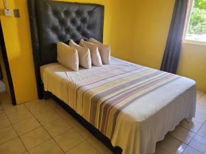a bed with a black headboard and three pillows at Enchanted Guest House & Hostel in Ocho Rios