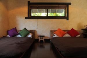 two beds with colorful pillows in a room with a window at Taketomijima Akaneya in Taketomi