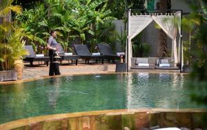 a man is standing next to a swimming pool at Central Indochine d'Angkor Hotel in Siem Reap