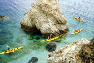 three people in kayaks in the water near a rock at Hotel Paradiso in Portoferraio