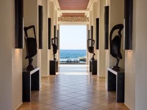 ein Flur mit ausgestellten Skulpturen vor dem Meer in der Unterkunft Amirandes, A Resort to Live in Gouves