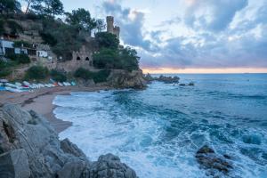 a beach with rocks and a castle in the distance at Apartamento Marina in Lloret de Mar