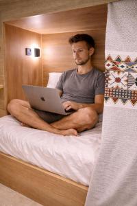 a man sitting on a bed with a laptop at 12H Hostel in Al-ʿUla