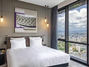 a bedroom with a white bed and a large window at Pullman Tbilisi Axis Towers in Tbilisi City