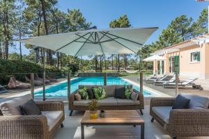 a patio with two couches and an umbrella next to a pool at Villa Buganvilia III in Aroeira