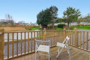 two white chairs sitting on a wooden deck at Lakeside Nest - Fishing Lakes, Heated Outdoor Swimming Pool 500yrds on Sister Park , Pool Open May to September in Exeter