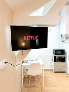 a tv on a wall above a white table with a chair at Studio Prestige, Cocon de Charme & Confort in Saint-Quentin
