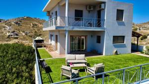a house with a balcony with chairs and a lawn at Villa Kalli - Porto Ennia in Vromopoúsi