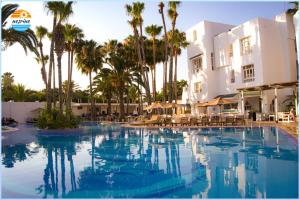 ein großer Swimmingpool vor einem Gebäude mit Palmen in der Unterkunft Hotel Nesrine Hammamet in Hammamet