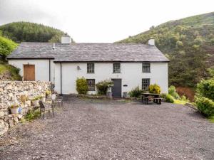 a white house with a stone wall and a patio at Cwm Ffernol in Machynlleth