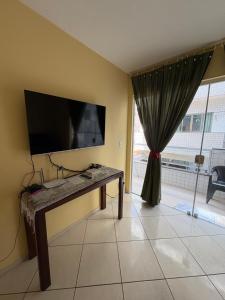 a living room with a table and a tv on a wall at Apartamento do Lala in Arraial do Cabo