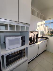 eine Küche mit weißen Schränken und einer Mikrowelle in der Unterkunft Apartamento em Maringá zona 07, próximo da universidade UEM in Maringá