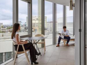 a man and woman sitting in chairs in a room with windows at Aparthotel Adagio London Brentford in Brentford