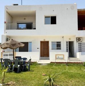 a white house with chairs and an umbrella in the yard at Bord de Mer kelibia ezzahra in Ḩammām al Ghazzāz