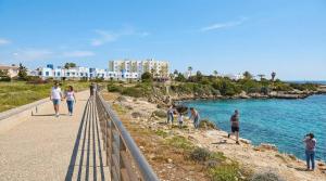 a group of people standing on a path near the water at Coralli Beachfront 1BDR Protaras in Paralimni