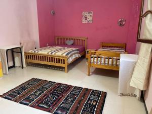 two beds in a room with pink walls and a rug at Adam House in Ghardaïa