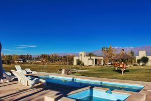 a swimming pool with two white chairs and a yard at Complejo Piuquenes Valle de Uco in Vista Flores