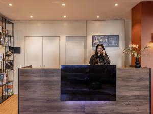 a woman standing behind a counter talking on a cell phone at Ibis Sion in Sion