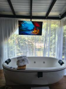 a white bath tub in front of a window with a tv at Cabana Recanto Dona Ilza in Biguaçu
