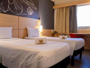 zwei Betten in einem Hotelzimmer mit weißer Bettwäsche in der Unterkunft ibis Macae in Macaé