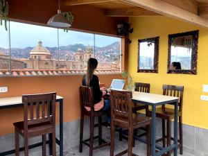 a woman sitting at a table with a laptop looking out a window at Maytaq Wasin Boutique Hotel in Cusco