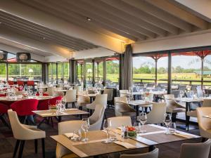 a restaurant with tables and chairs and windows at Cabot Hotel Bordeaux - MGallery Collection in Le Pian-Médoc