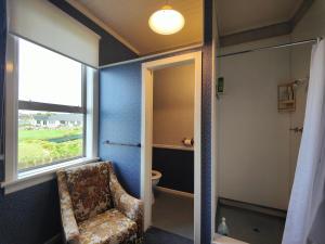 a bathroom with a chair and a window and a toilet at Justavacation Beachfront Bach in Riverton +15 photos