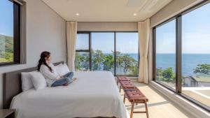 a woman sitting on a bed in a room with large windows at Pohang Sausalito by B-Class Pool Villa in Pohang