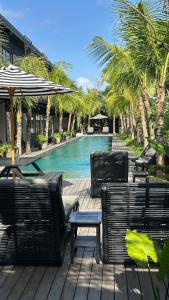 a pool with chairs and an umbrella and a table at Koji Collection in Kerobokan