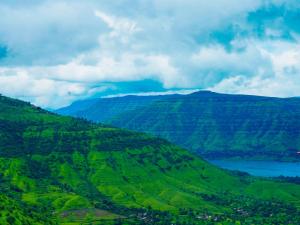 a view of a green mountain with a lake at Hotel Prathamesh in Panchgani
