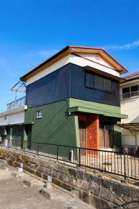 a green and black house with a fence at ゲストハウス元町 in Ise