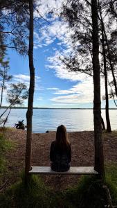 a woman sitting on a bench looking at the water at MELLOW TREES Lake front studio with sauna in Budgewoi