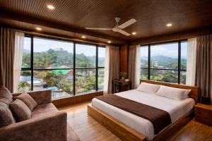 a bedroom with a bed and a couch and large windows at Dolphin Residency in Thekkady