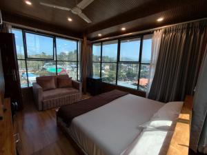 a bedroom with a bed and a chair and windows at Dolphin Residency in Thekkady