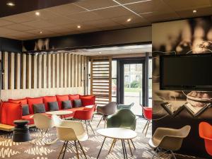a lobby with red chairs and tables and a flat screen tv at ibis Troyes Centre in Troyes