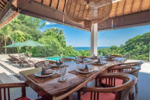a long wooden table with chairs and a view of the ocean at Villa Bayu - exclusive villa with infinity pool, wellness pavilion, panoramic ocean view & full service in Temukus