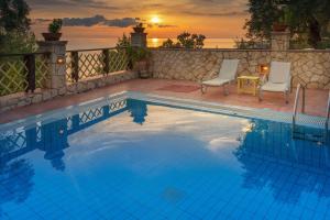 a swimming pool with two chairs and a sunset in the background at Zakynthos Villas in Vasilikos